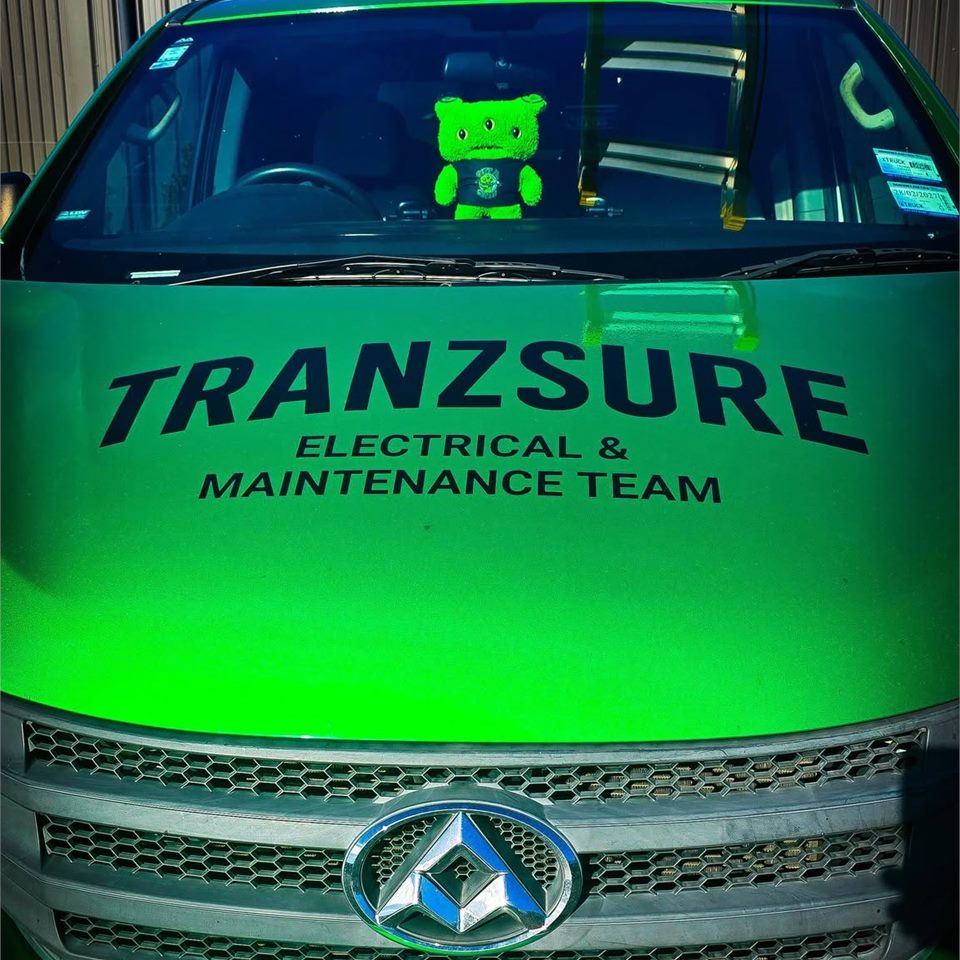 The front of the bright green Tranzsure van, signwritten Electrical & Maintenance Team, with the green plush mascot sitting on the dashboard