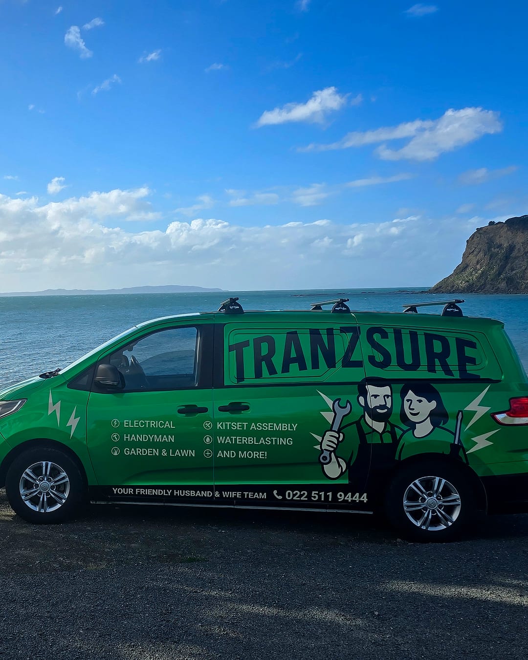 The bright green Tranzsure van parked above a beach, with the sea and a headland behind it